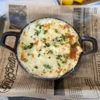 Golden baked cheesy food in black cast-iron dish with herbs.