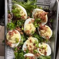 Deviled eggs with bacon and chives on lettuce, in newspaper-lined tray.