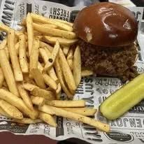 Close-up of a sloppy joe, golden fries, and a dill pickle.