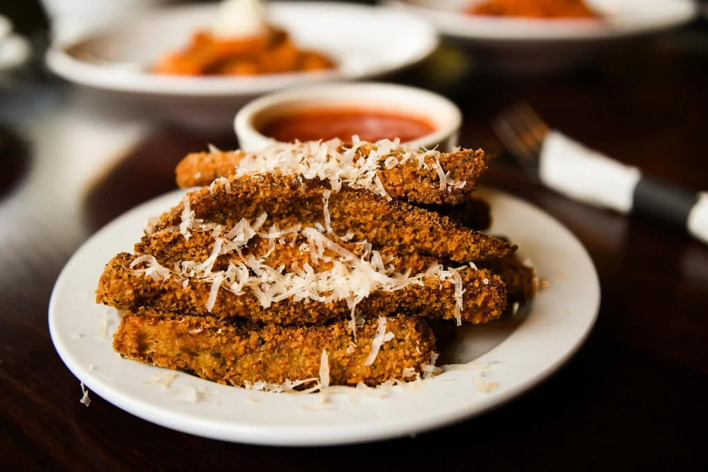 Plate of fried sticks with grated cheese and marinara in a restaurant.