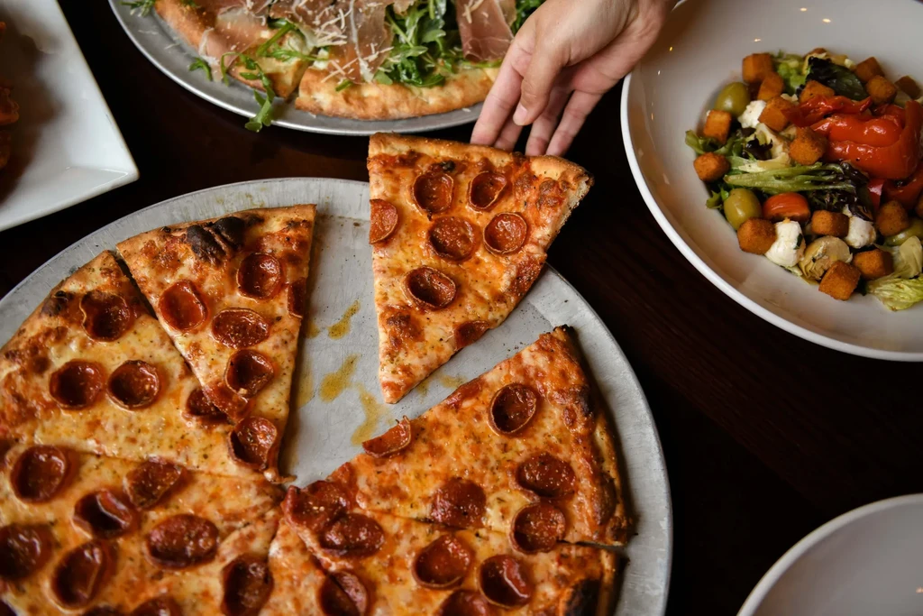 Overhead: Hand lifting pepperoni pizza slice, other food on table.
