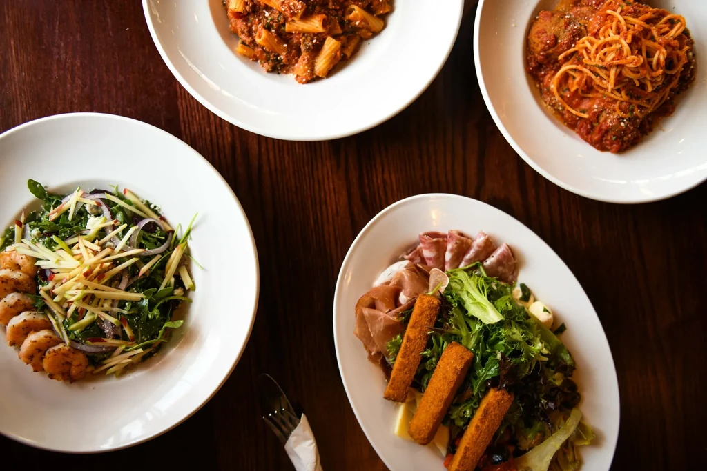Overhead view of four plated Italian dishes on a dark table.