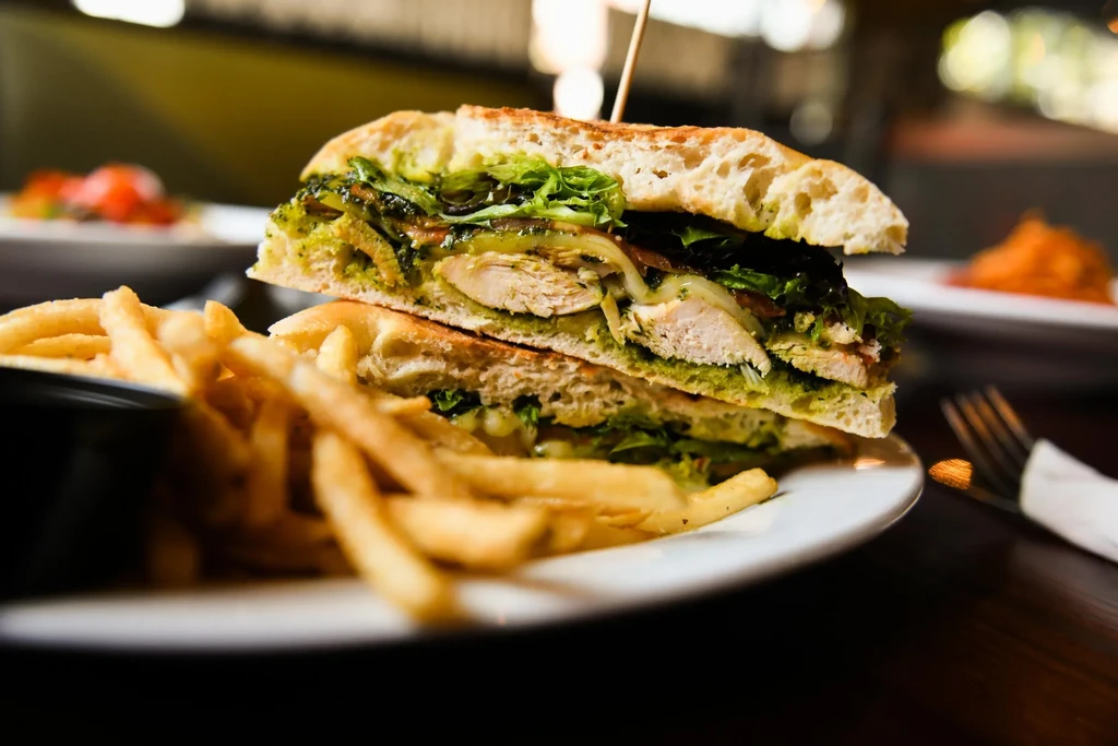 Half ciabatta chicken pesto sandwich and golden-brown french fries.