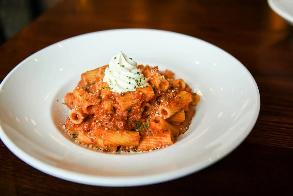 Rigatoni with red sauce, creamy ricotta, green herbs in white bowl.