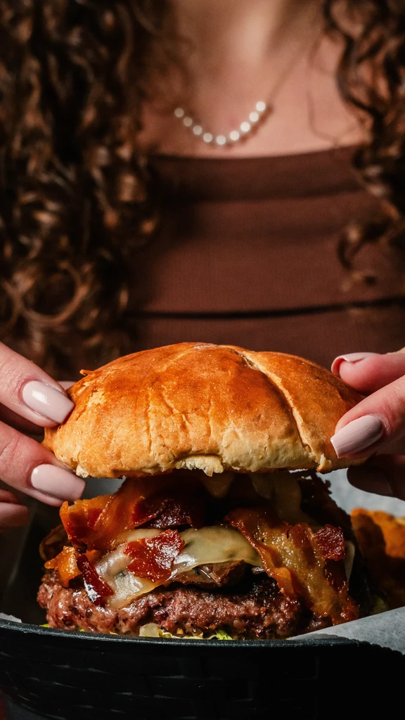Low-angle close-up of hands holding a generous bacon cheeseburger.