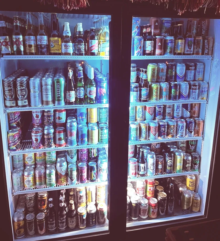 Large two-door cooler stocked with diverse bottled and canned drinks.