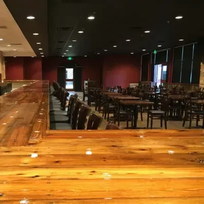 Empty, dim restaurant interior with wooden bar, tables, and maroon walls.