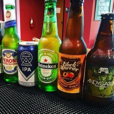 Four beer bottles and one can on a black bar mat.