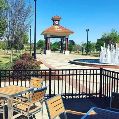 Empty restaurant patio overlooks park with a gazebo and fountain.