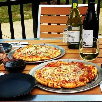 Two pizzas and wine on an inviting outdoor table setting.