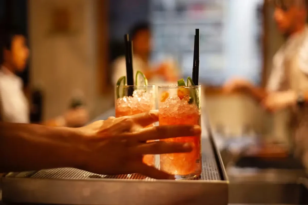 Two garnished cocktails with crushed ice and straws on a bar.