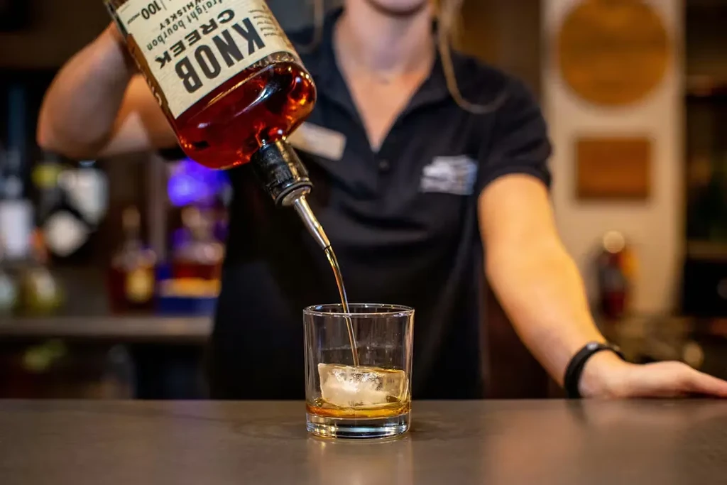 Bartender pours Knob Creek whiskey into a glass with ice.