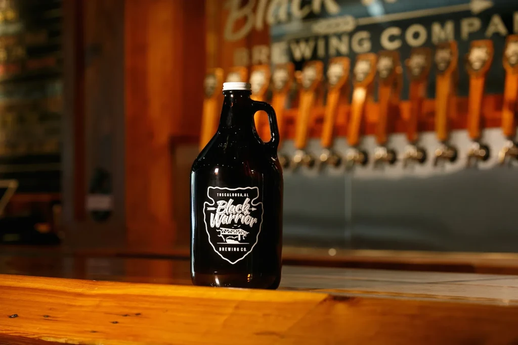 Dark brown growler with Black Warrior Brewing Co. label on a bar.