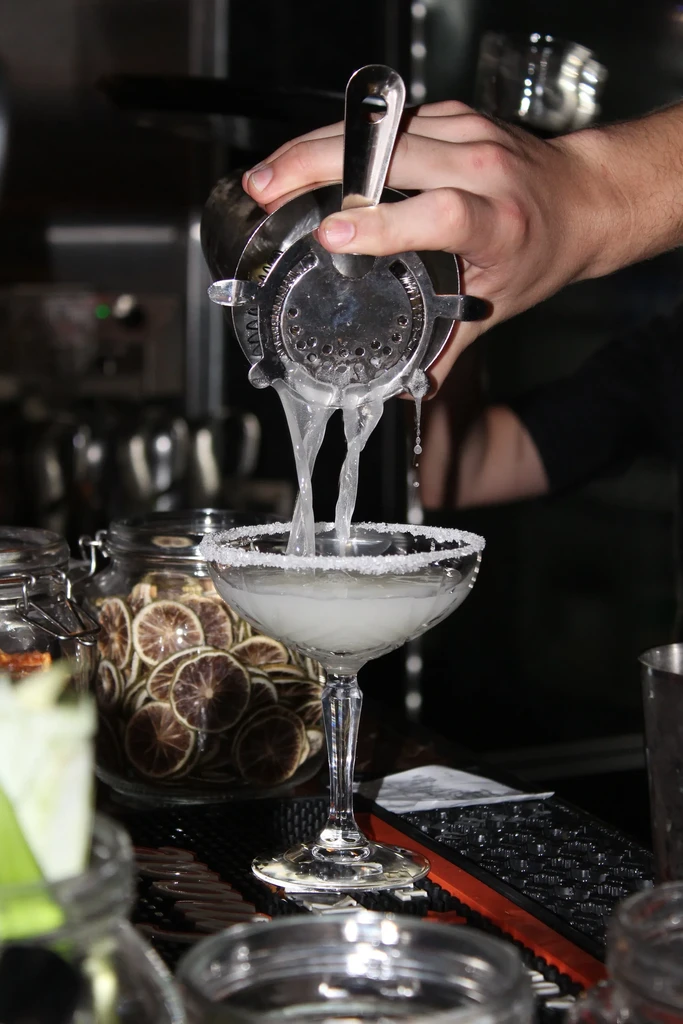Bartender's hands pour a cocktail through a strainer into a sugared glass.