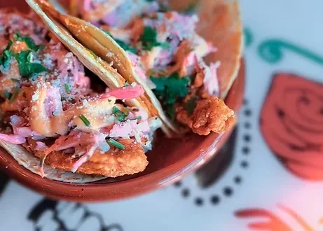 Two vibrant tacos with fried protein, pink slaw, and orange sauce.