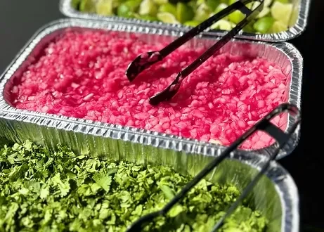 Aluminum trays with pickled red onions, cilantro, and lime wedges.