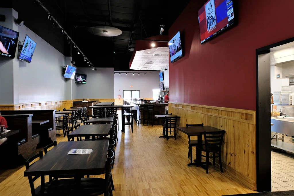 Casual restaurant interior with dark wood tables, bar, and TVs.