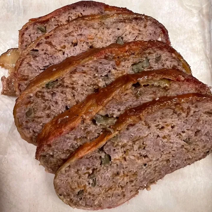 Five slices of glazed meatloaf with green vegetables on a platter.