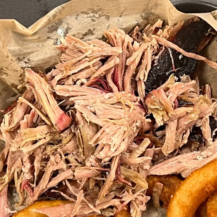Close-up of pulled pork with bark in a black container.