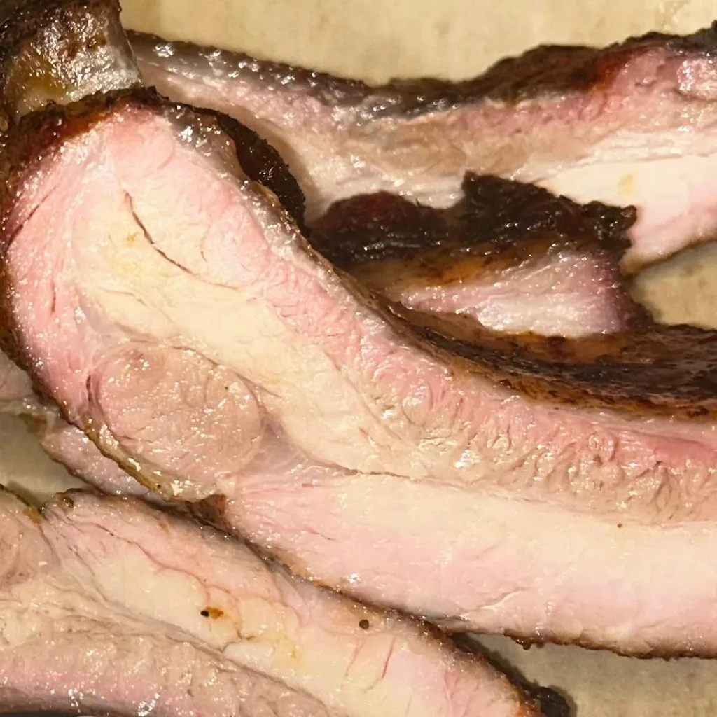 Cross-section of cooked meat slices with dark smoke ring and pink interior.