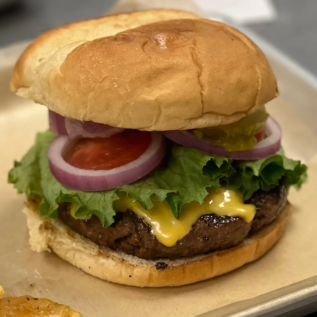 Burger with bun, thick patty, melted cheese, lettuce, tomato, onion.