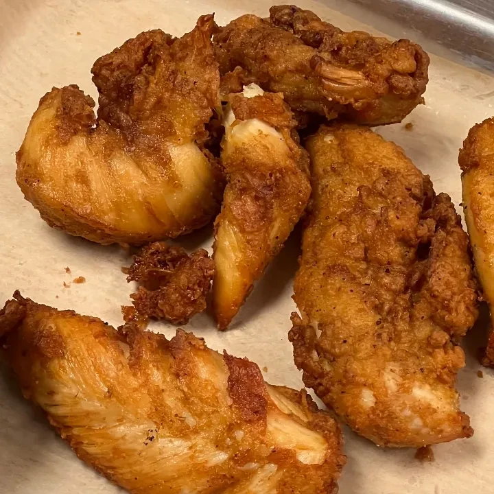 Golden-brown fried chicken pieces with crispy breading on light paper.