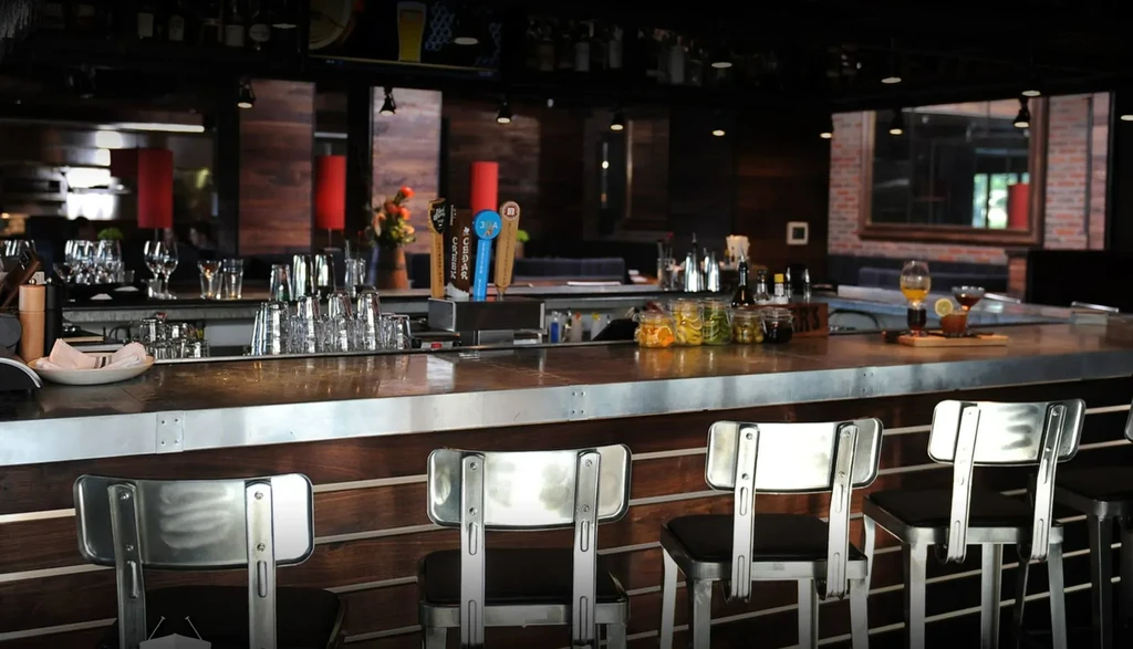 Empty modern bar with metallic counter, beer taps, garnishes, and drinks.