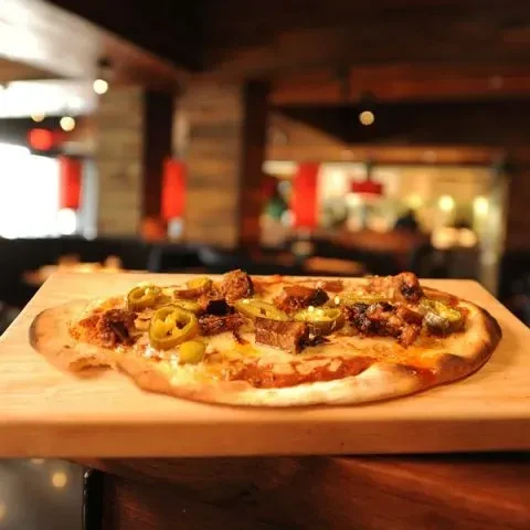 Charred rustic meat and jalapeño pizza on a wooden paddle.