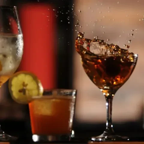 Three cocktails on a bar, one splashing from a coupe glass.