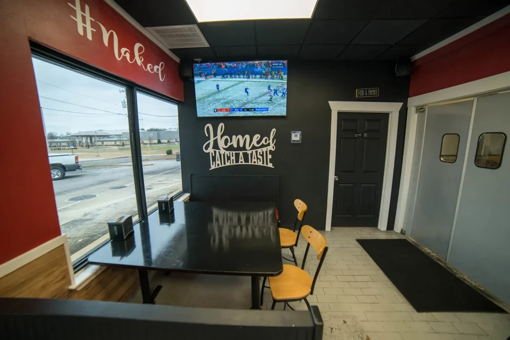 Casual restaurant interior with booth, TV showing football, and street view.