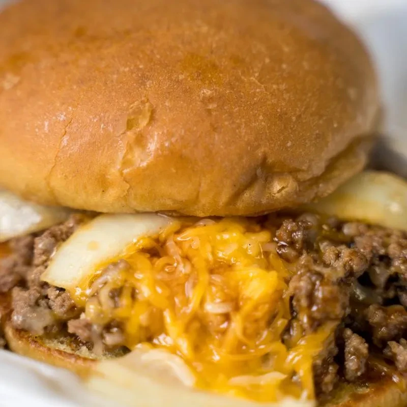 Close-up of a burger with ground meat, melted cheese, and onions.