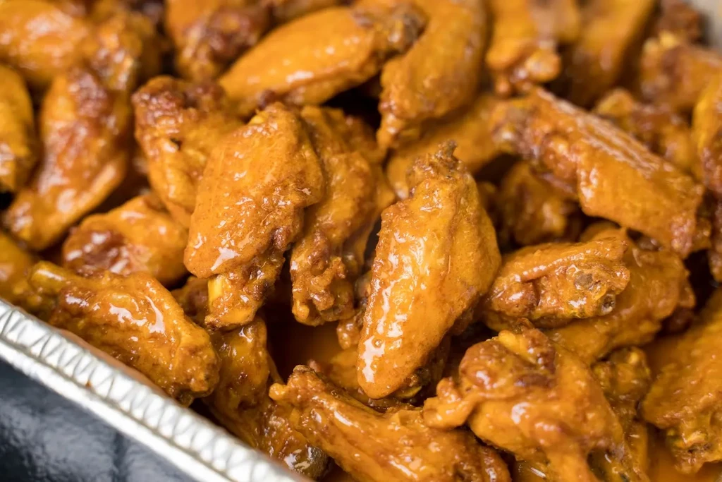 Cooked chicken wings with glossy reddish-orange sauce in an aluminum tray.