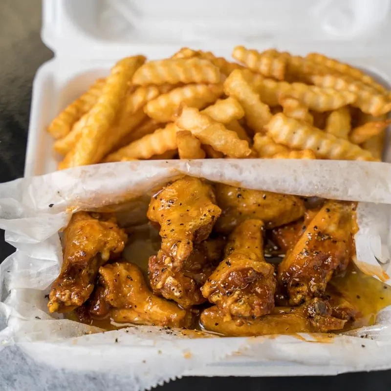 Take-out box with golden crinkle fries and reddish-orange glazed chicken wings.