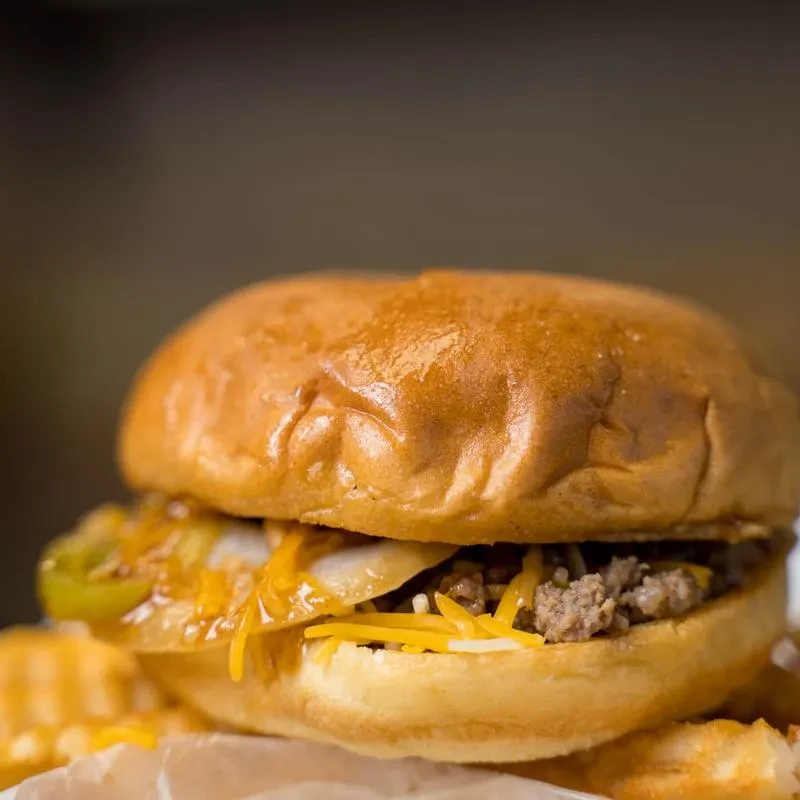 Close-up of a loaded burger with cheddar, jalapeños, onions, and fries.