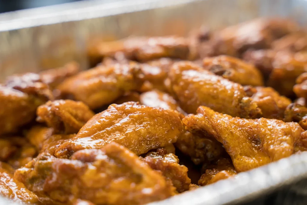 Close-up of golden-brown chicken wings with glistening sauce in a foil pan.