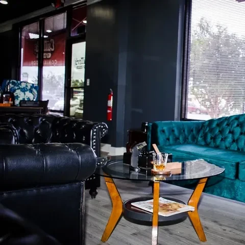 Upscale lounge with black and teal sofas, drink and cigar on table.
