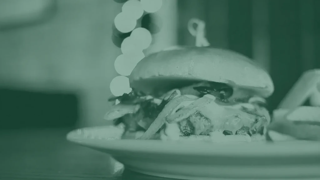 Green-filtered close-up of a substantial burger with fries on a plate.