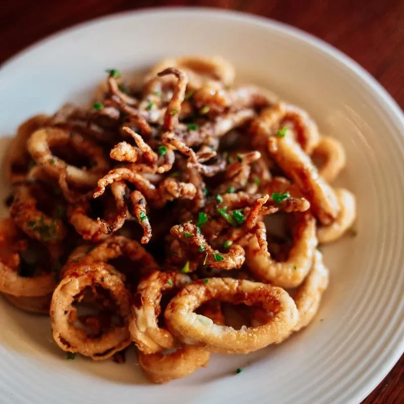 Crispy golden-brown fried calamari with fresh herbs on a plate.