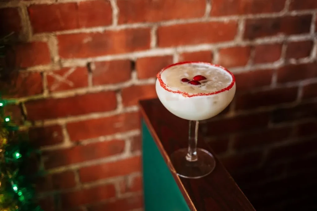 Single creamy white cocktail in coupe with red berries and rim.