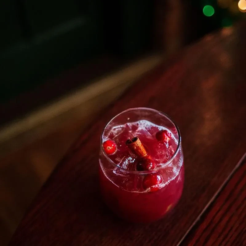 Reddish-purple cocktail with ice, cranberries, and a cinnamon stick.
