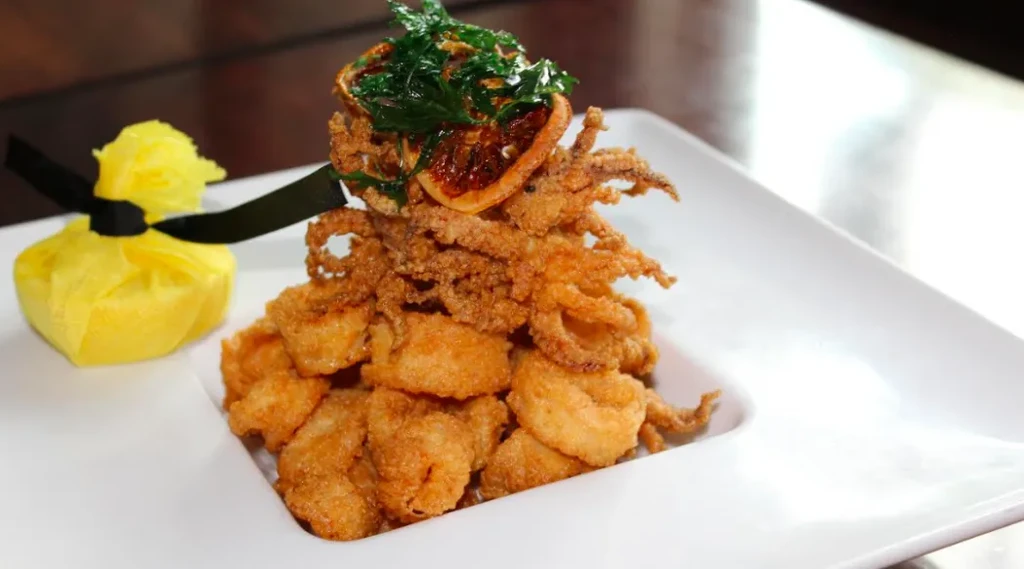 Golden fried calamari, citrus slice, and green herbs on a white plate.