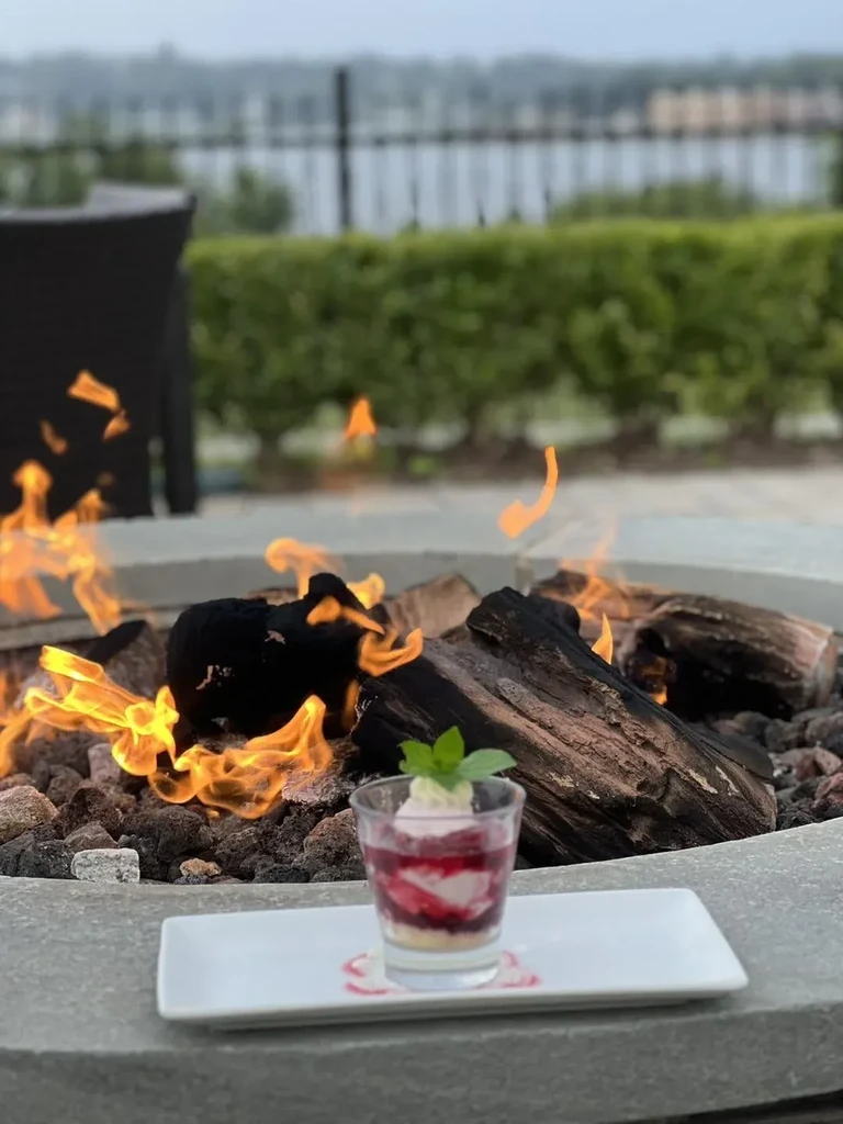 Layered fruit and cream dessert in glass, fire pit glowing behind.