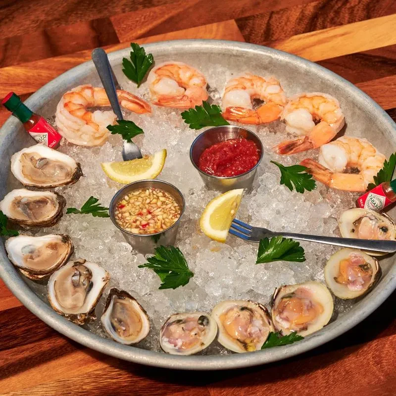 Seafood platter on ice with shrimp, oysters, clams, sauces, and lemons.