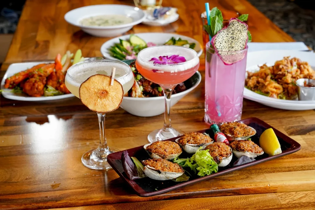 Baked clams and three vibrant cocktails on a restaurant table.