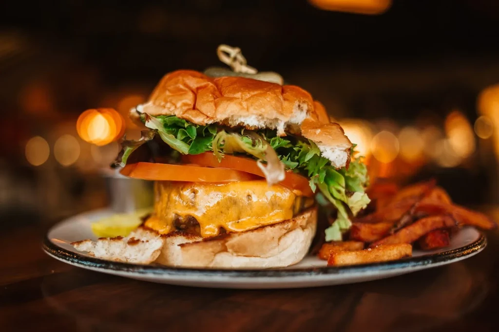 Close-up of a cheeseburger with melted cheese and sweet potato fries.