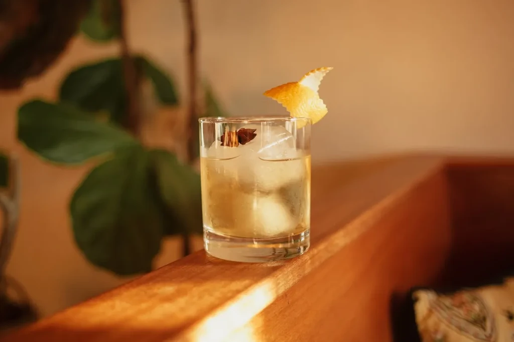 Amber cocktail with ice, citrus peel, and star anise on wood.