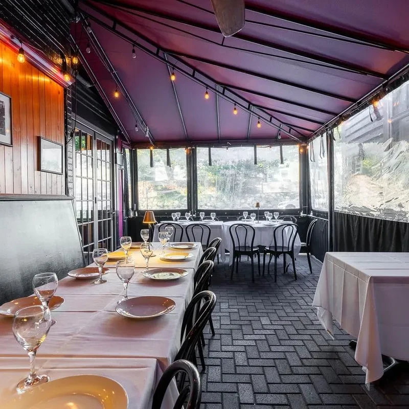 Indoor-outdoor restaurant dining with set tables, dark canopy, string lights.
