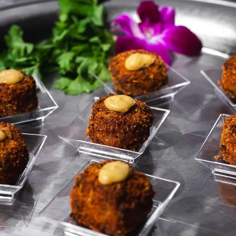 Croquettes with yellow sauce in individual dishes on a silver tray.