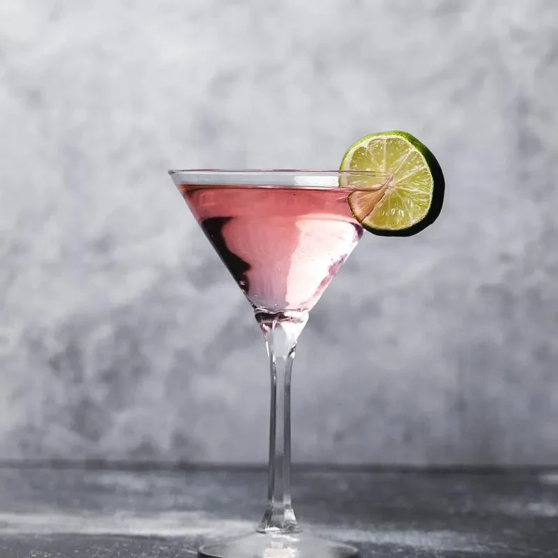 Pink martini cocktail with lime slice on a grey studio background.