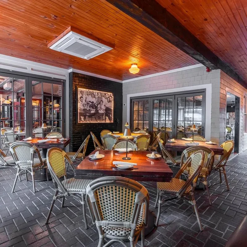 Restaurant with wooden ceiling, brick walls, dark tables, wicker chairs, warm lighting.
